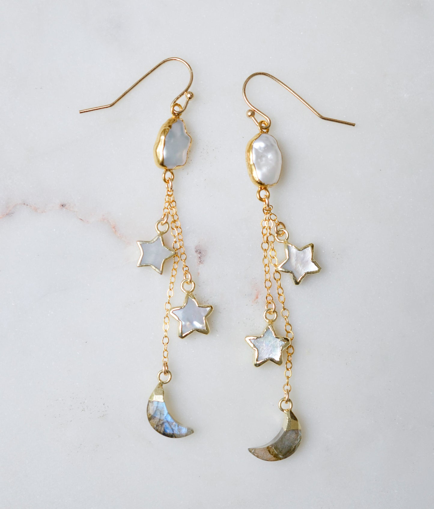 Long gold dangle earrings with star and moon charms on a light background. The stones are freshwater pearl, labradorite, and mother of pearl.