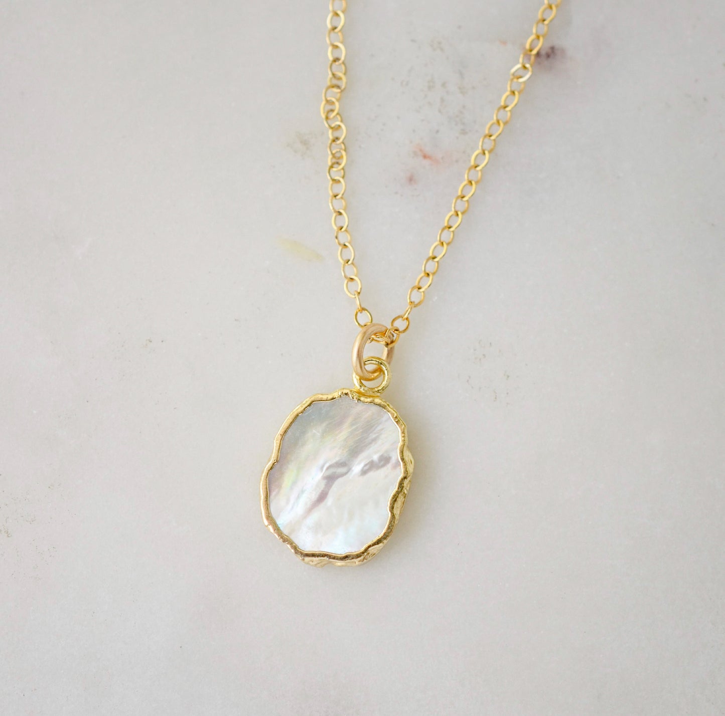 A smooth polished natural, white mother of pearl slice has been set in a 24k gold electroplated bezel and suspended from a 14k gold filled chain. The shell shimmers in shades of white, silver, and pink.