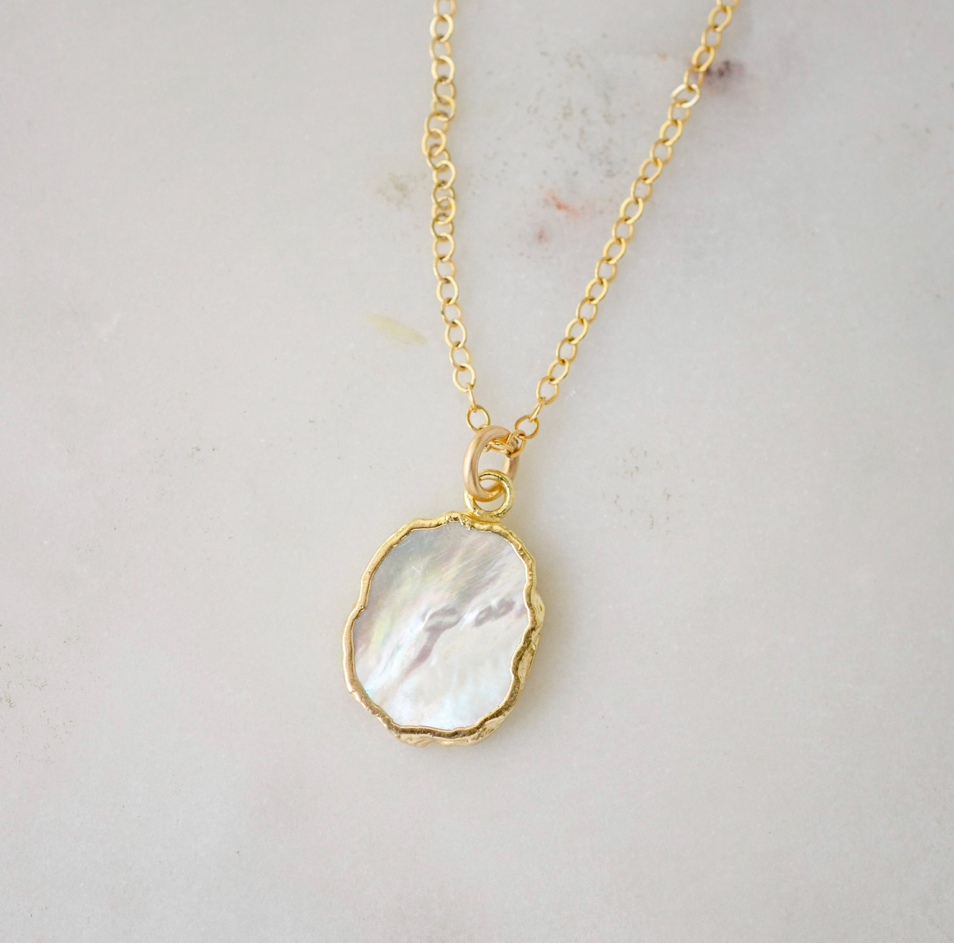 A smooth polished natural, white mother of pearl slice has been set in a 24k gold electroplated bezel and suspended from a 14k gold filled chain. The shell shimmers in shades of white, silver, and pink.
