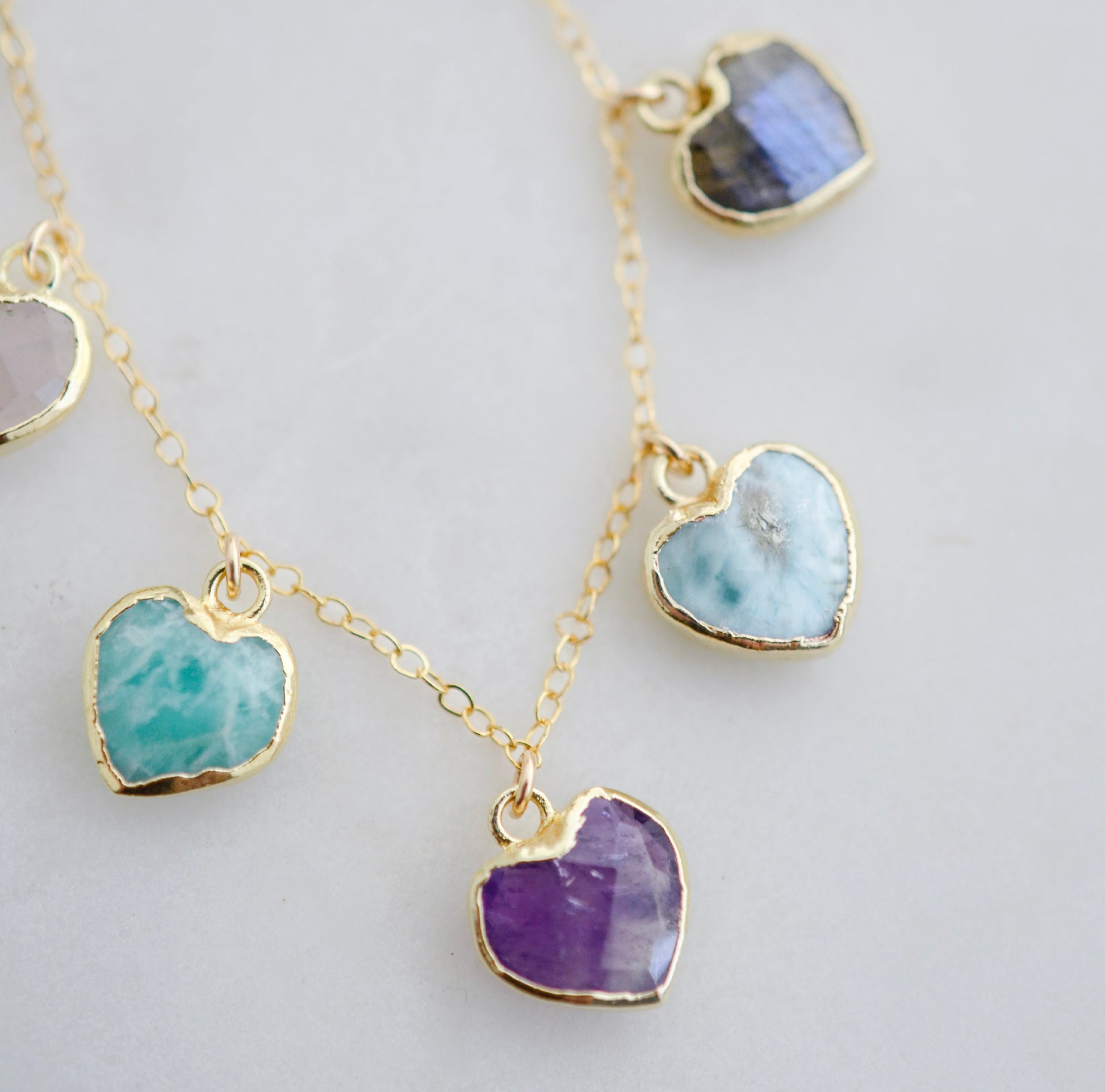 Close up image: Handmade dainty heart necklace with heart-shaped gemstones on a 14k gold filed chain. Stones include: Aquamarine, Rose Quartz, Amazonite, Larimar, Labradorite, Amethyst, and Rainbow Moonstone