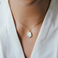 Modeled image. A smooth polished natural, white mother of pearl slice has been set in a 24k gold electroplated bezel and suspended from a 14k gold filled chain. The shell shimmers in shades of white, silver, and pink.