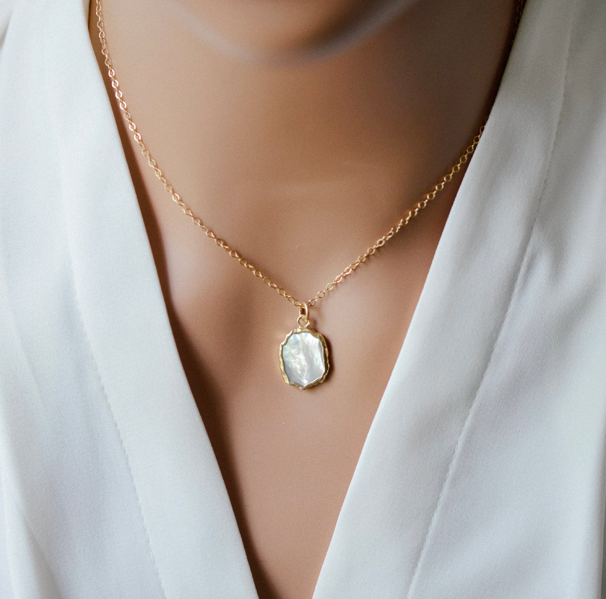 Modeled image. A smooth polished natural, white mother of pearl slice has been set in a 24k gold electroplated bezel and suspended from a 14k gold filled chain. The shell shimmers in shades of white, silver, and pink.