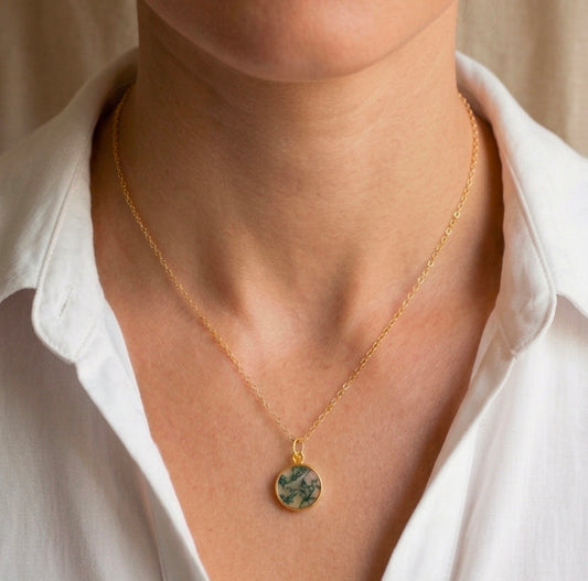 Modeled image of a small, natural moss agate circle pendant set on a 14k gold filled chain. This minimalist, delicate, smooth polished pendant is handmade in Connecticut by Gemnia Jewelry. Also available in sterling silver.