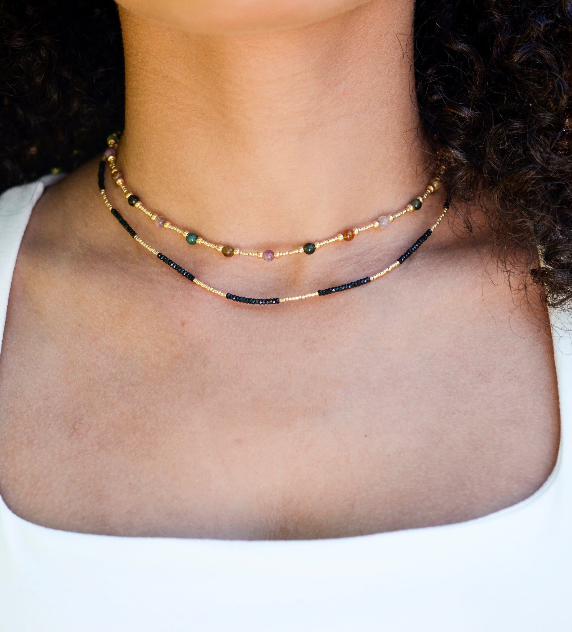 Multicolored, smooth polished Tourmaline gems hand-beaded with gold plated glass beads. Colors range from pink, green, brown, yellow, or black. Modeled image. Modeled with a black onyx beaded necklace.