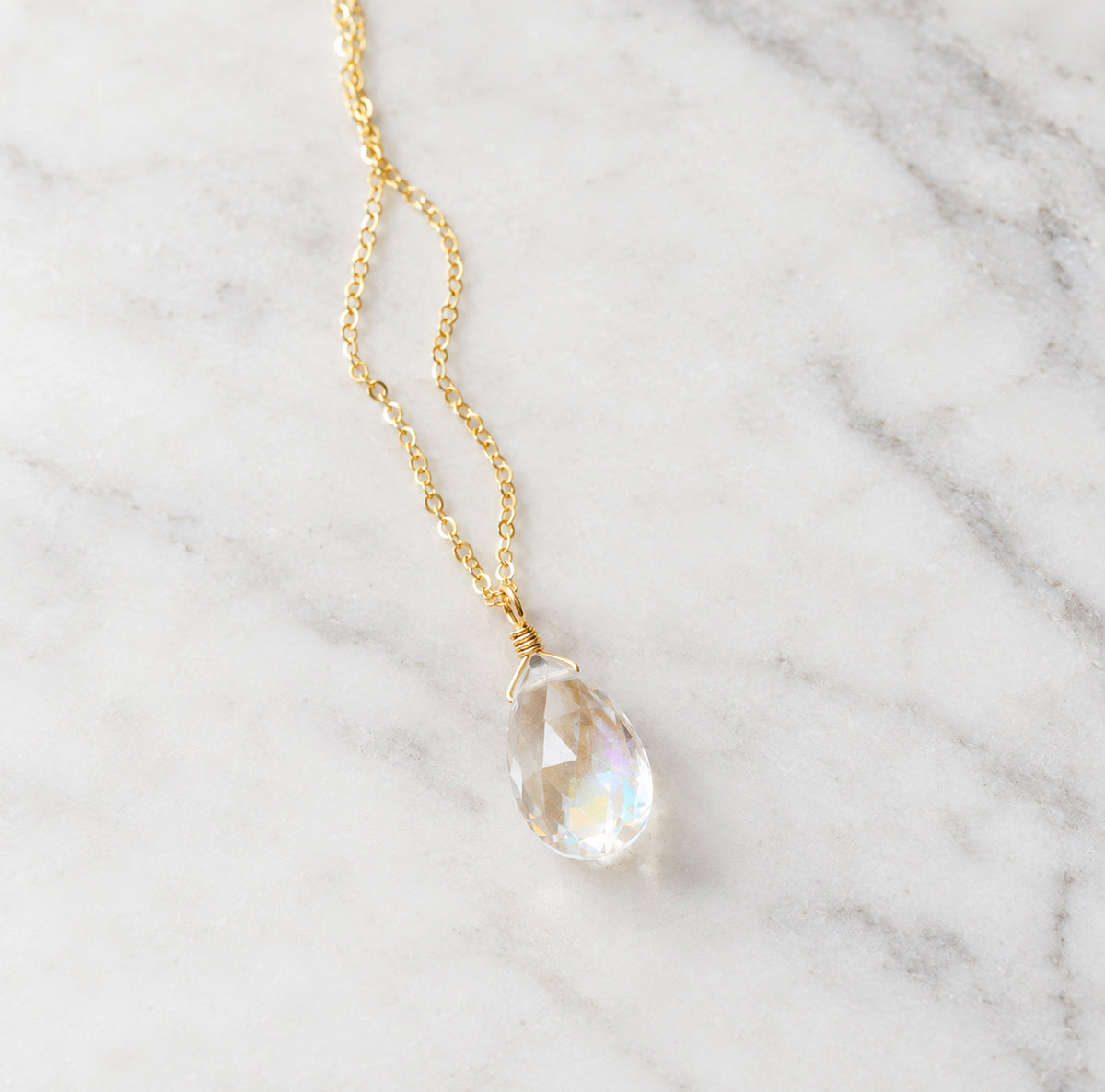 A faceted mystic topaz gemstone set on a dainty 14k gold filled chain. The stone is clear, but shimmers rainbow colors when turned from side to size. This pendant is handmade in Connecticut by Gemnia.