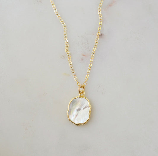 A smooth polished natural, white mother of pearl slice has been set in a 24k gold electroplated bezel and suspended from a 14k gold filled chain. The shell shimmers in shades of white, silver, and pink.