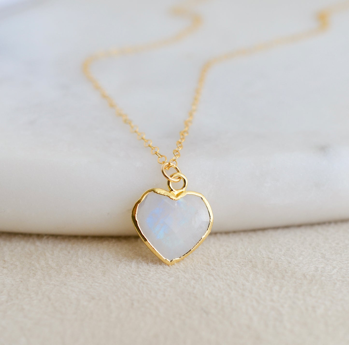 Genuine natural rainbow moonstone romantic heart gemstone pendant set on a dainty 14k gold filled cable chain. Close up image showing the blue flash within the gemstone. 