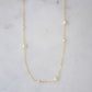 Gold necklace with small dainty pearls on a marble surface.