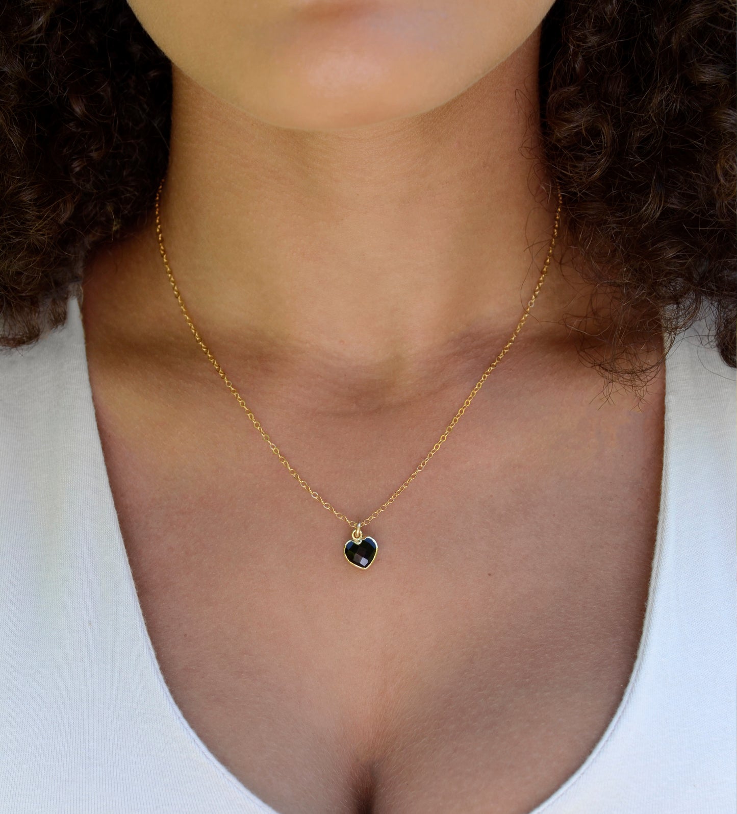 Black Onyx gold heart necklace. A black stone heart bezeled in gold is suspended from a 14k gold filled chain. Modeled image.