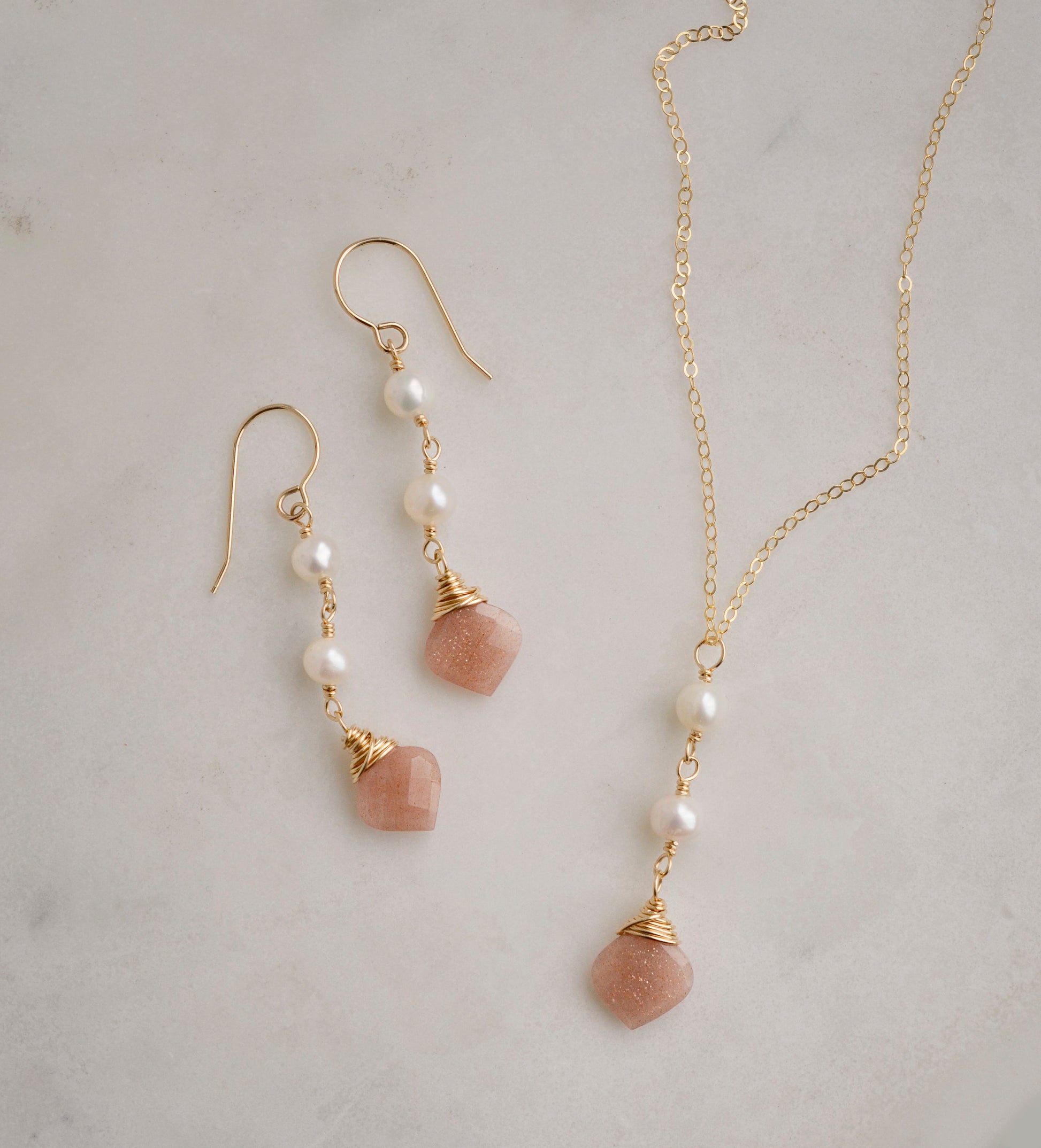 Two white semi-round pearls hang over a natural peach Moonstone faceted drop. The gold style pendant is shown with the matching earrings.