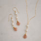 Two white semi-round pearls hang over natural peach Moonstone faceted drops. Shown with a matching necklace. The gold style is shown.
