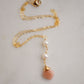 Two white semi-round pearls hang over a natural peach Moonstone faceted drop. The gold style pendant is shown.