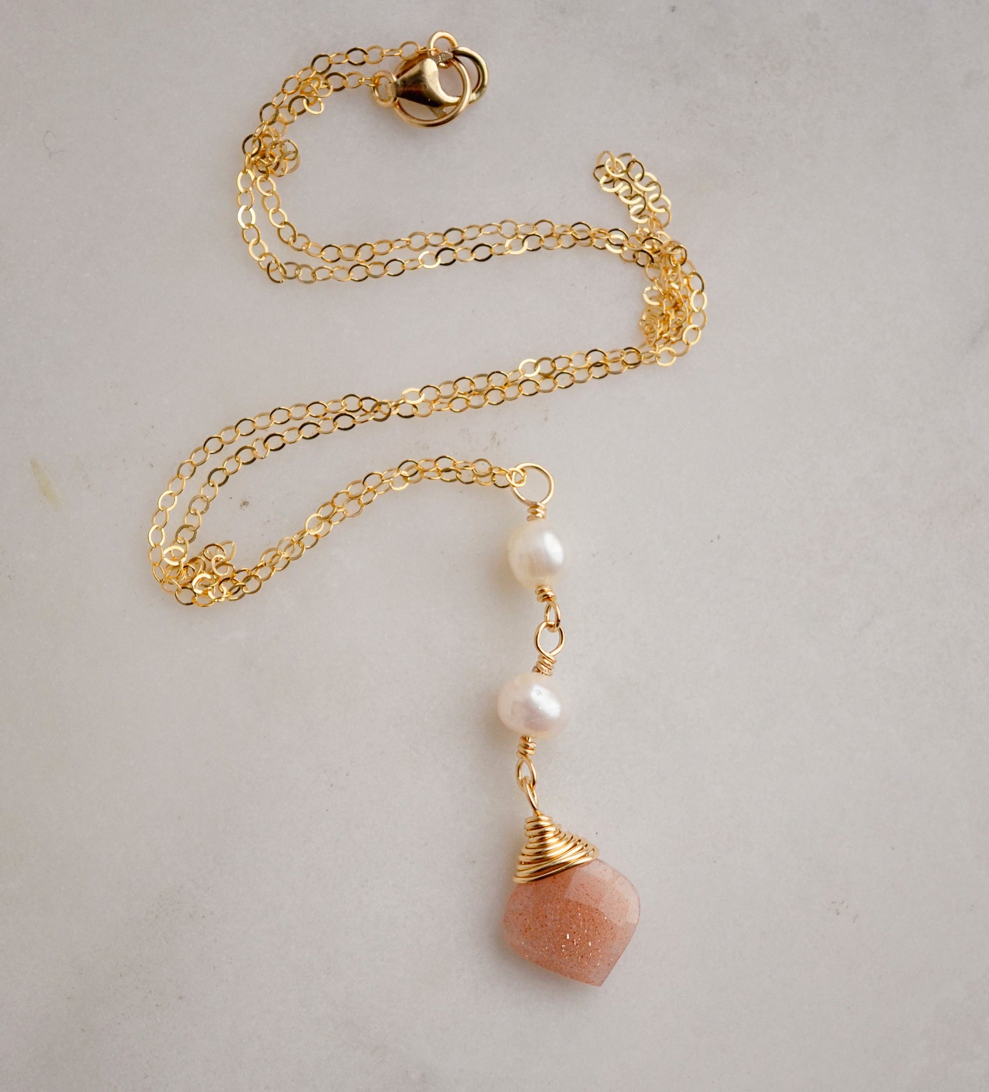 Two white semi-round pearls hang over a natural peach Moonstone faceted drop. The gold style pendant is shown.