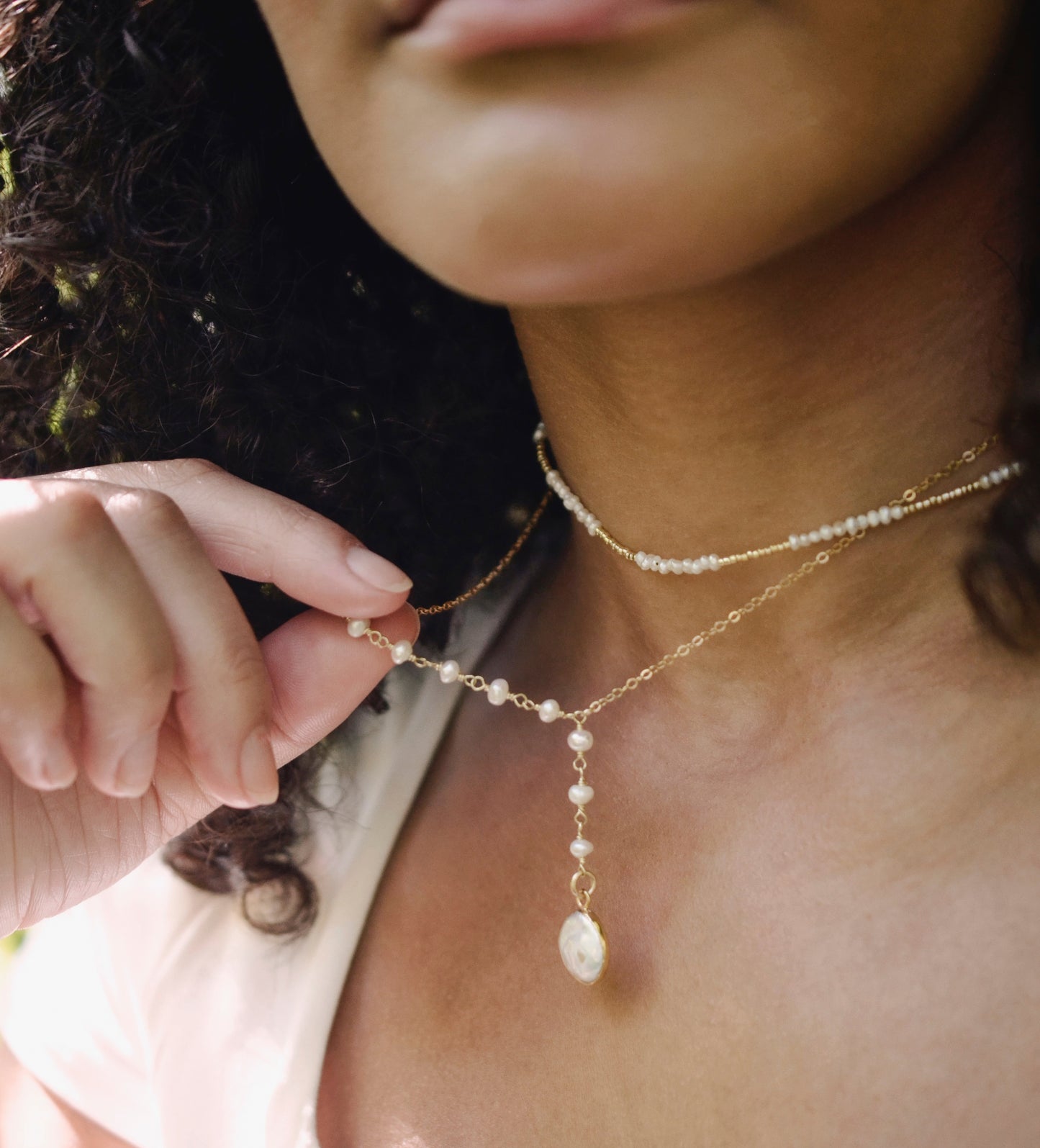 White freshwater pearl necklace with a large coin pearl pendant. Pearls fill one side of the necklace, while the other side is a dainty gold chain. Modeled image.