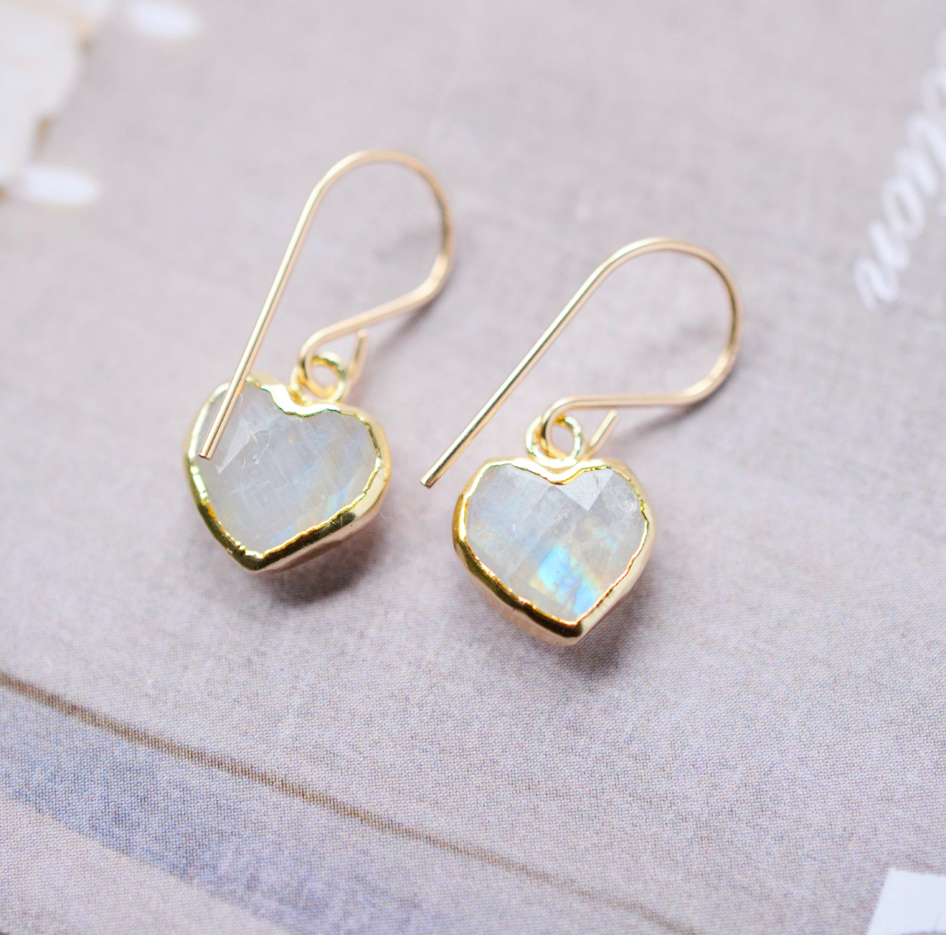 Natural rainbow moonstone stone heart earrings in gold. The stones are white, but flash blue with movement.