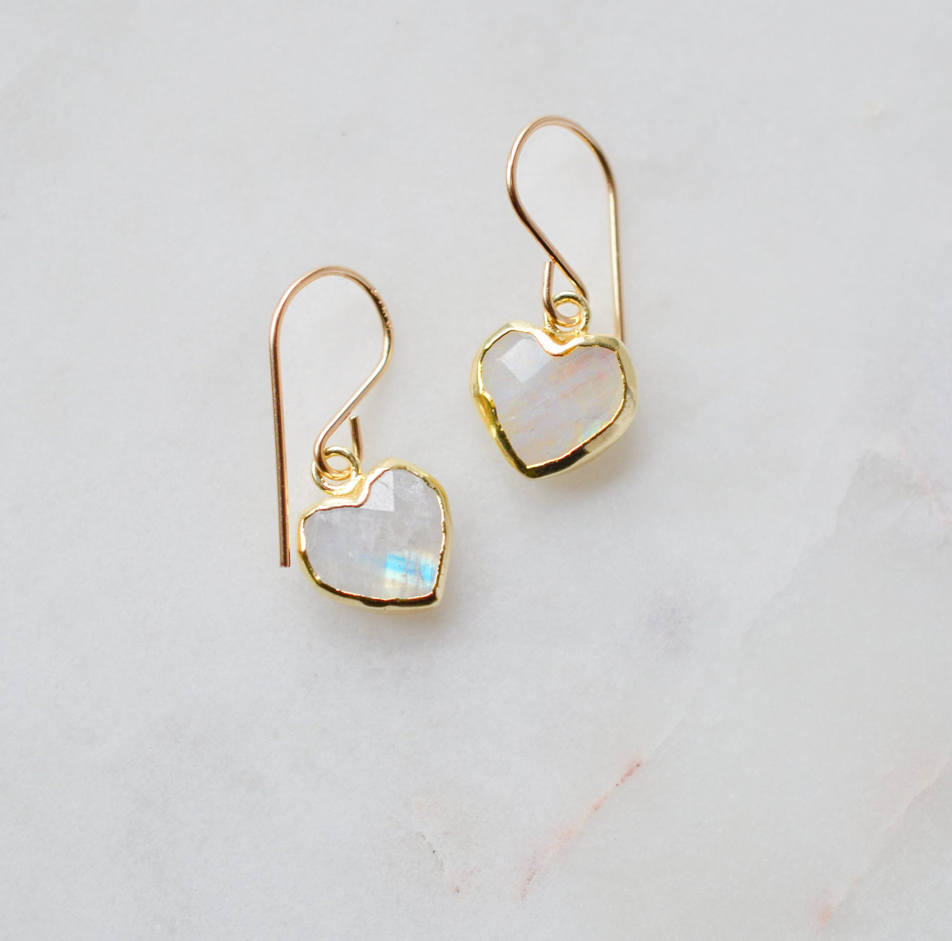 Natural rainbow moonstone stone heart earrings in gold. The stones are white, but flash blue with movement.