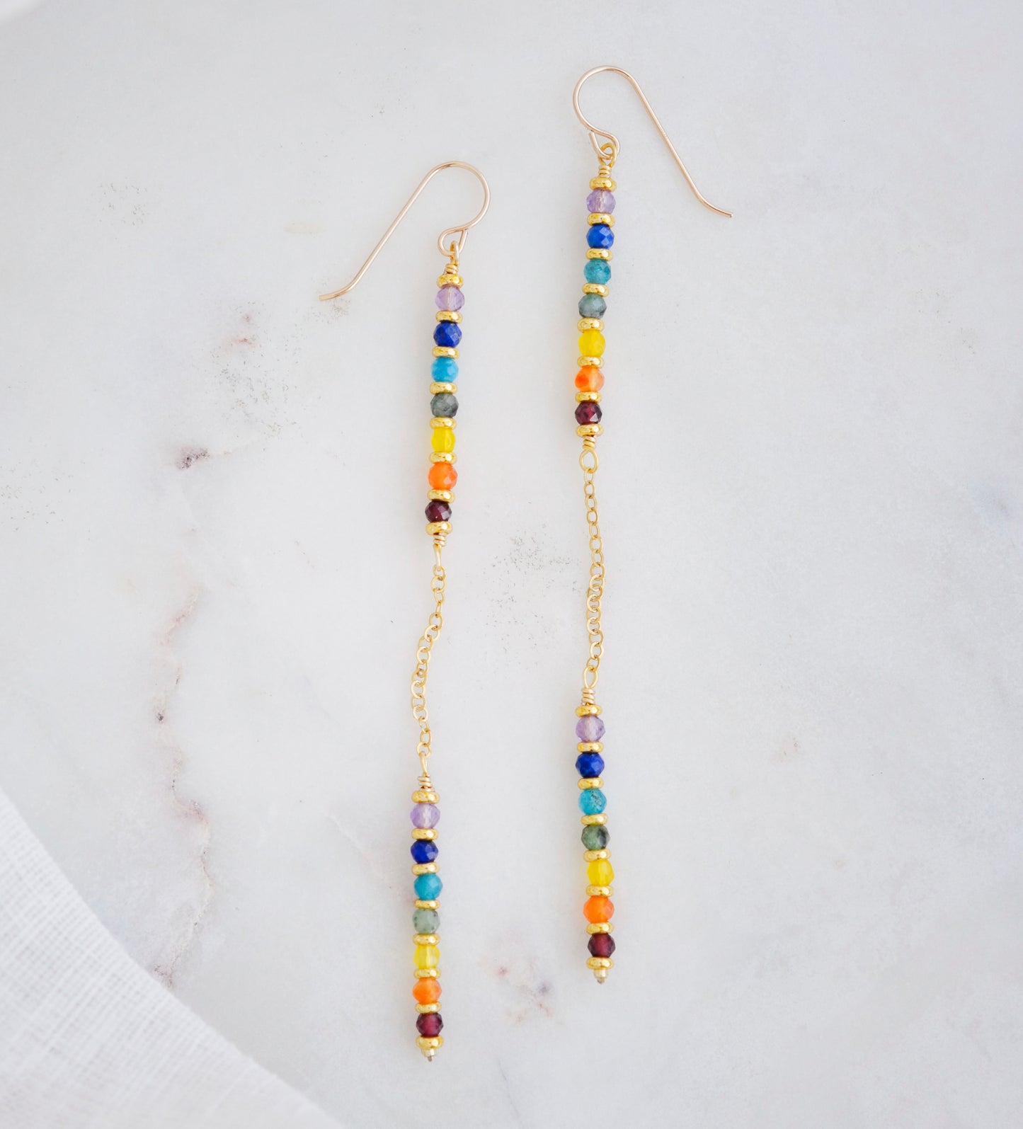 Two long, straight bars of crystals arranged in a rainbow pattern separated by a dainty chain. The gold style is shown showing the flexible chain.