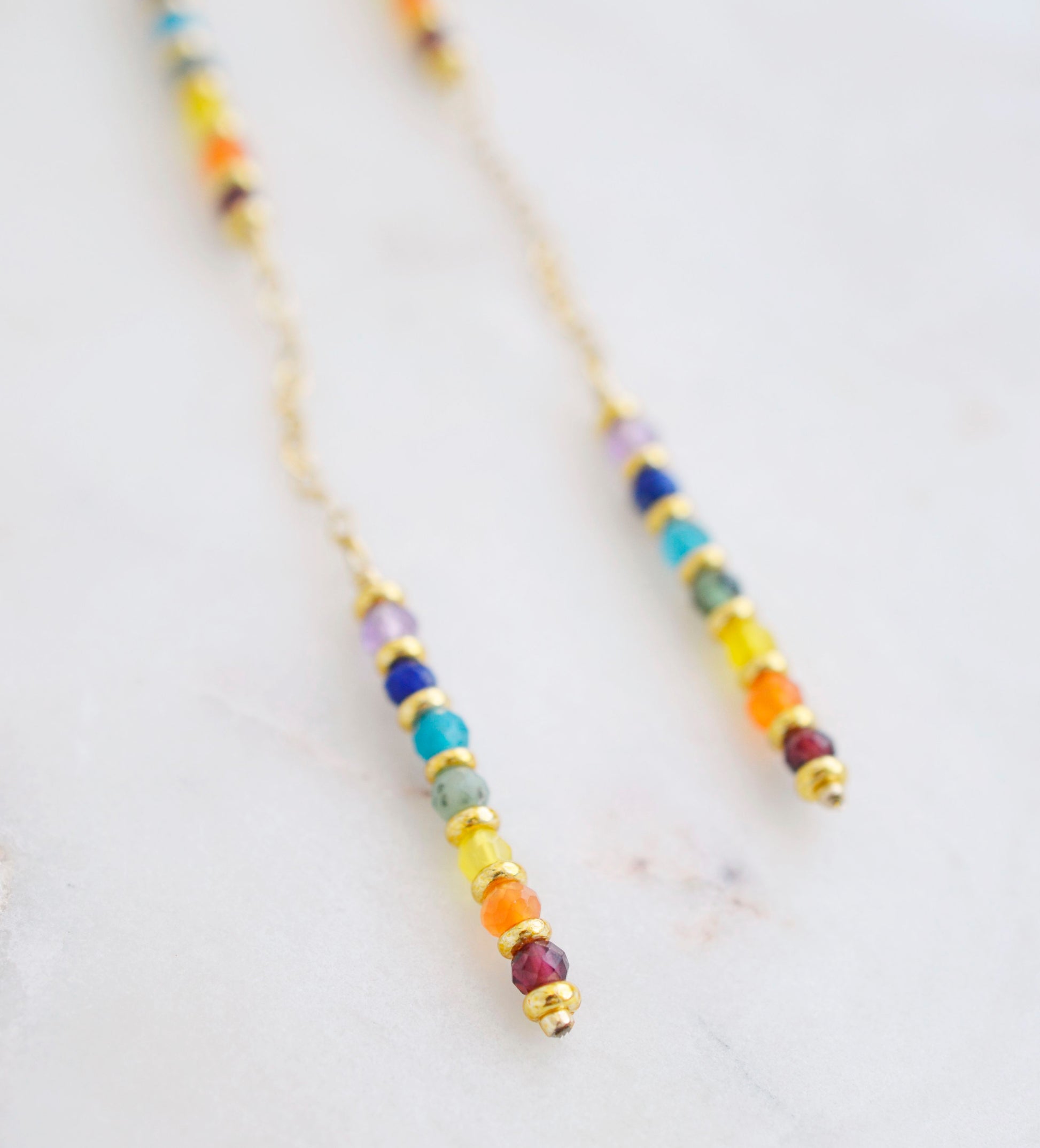 Close up. Two long, straight bars of crystals arranged in a rainbow pattern separated by a dainty chain. The gold style is shown. 