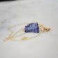 Raw blue lapis lazuli stone suspended from a gold chain.