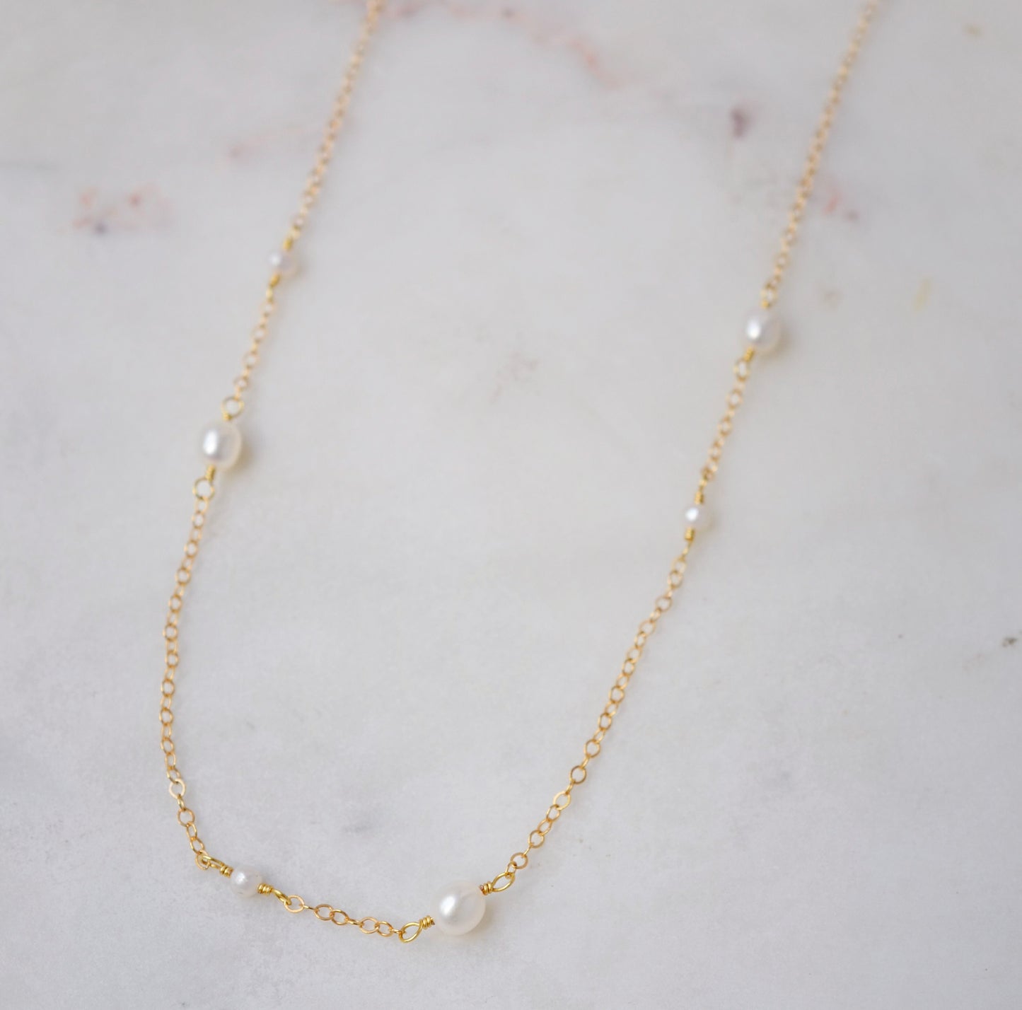 Natural white freshwater pearls of varying sizes on a dainty chain necklace. The gold style is shown.