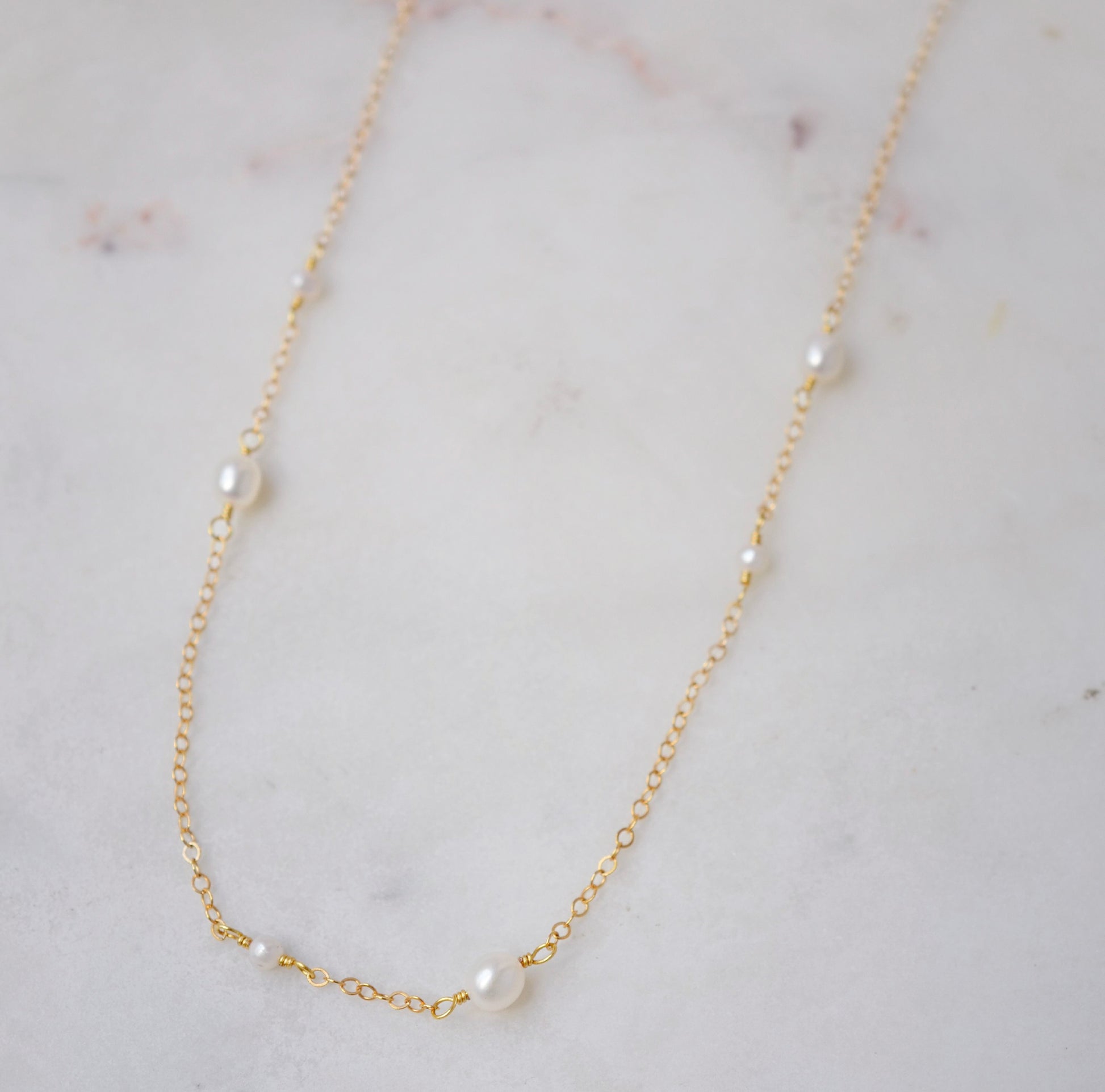 Natural white freshwater pearls of varying sizes on a dainty chain necklace. The gold style is shown.