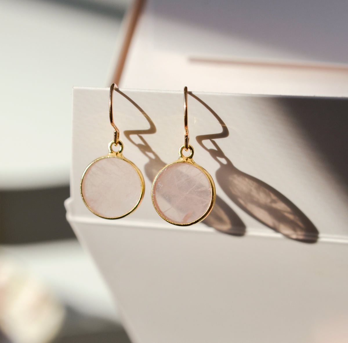 Natural pale pink rose quartz dangle earrings in a circle coin shape. The stones are smooth polished and are dainty, lightweight, and minimalist. 