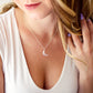 A woman wearing a natural rose quartz crescent moon necklace in sterling silver. The stone is genuine and faceted. Also available in 14k gold filled. 