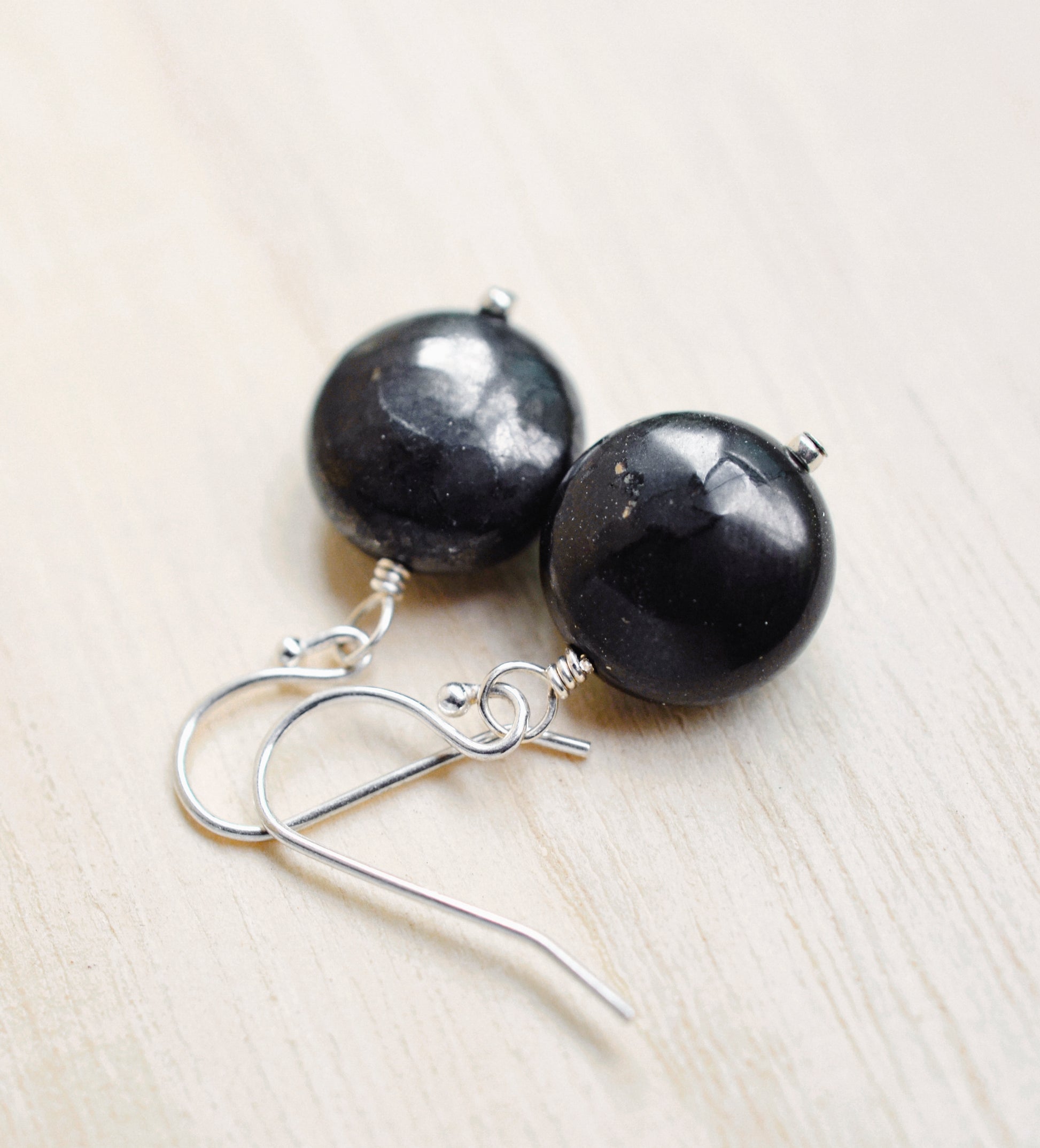 Natural smooth polished coin shape black Shungite dangle from sterling silver earring hooks.