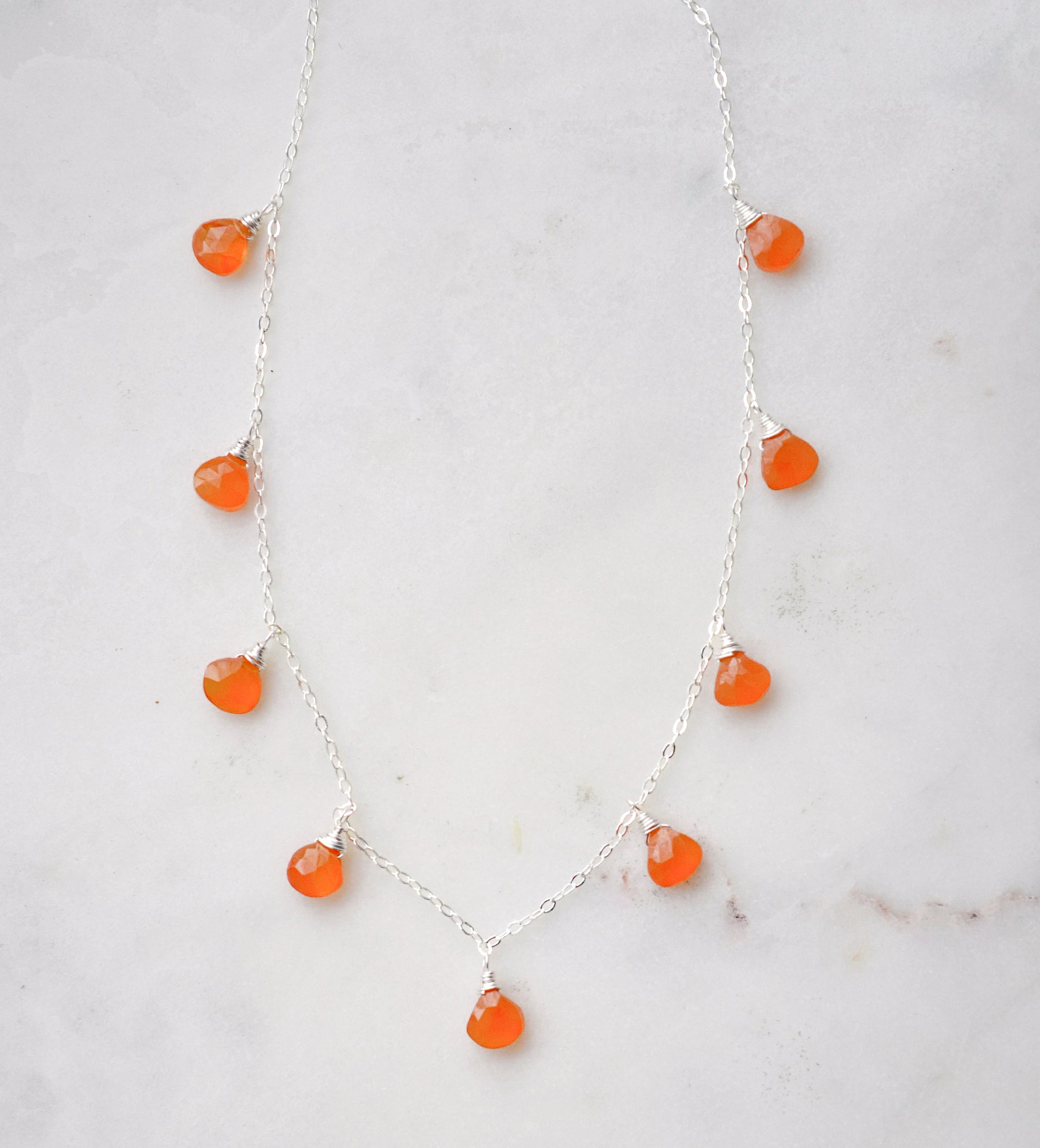 Multiple orange carnelian crystal gemstones dangle off a sterling silver chain.