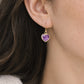 A woman wearing natural purple amethyst heart shaped dangle earrings in gold. The bezel is 18k gold electroplate and is organic in shape. The earwires are french hooks. Handmade jewelry by Gemnia.