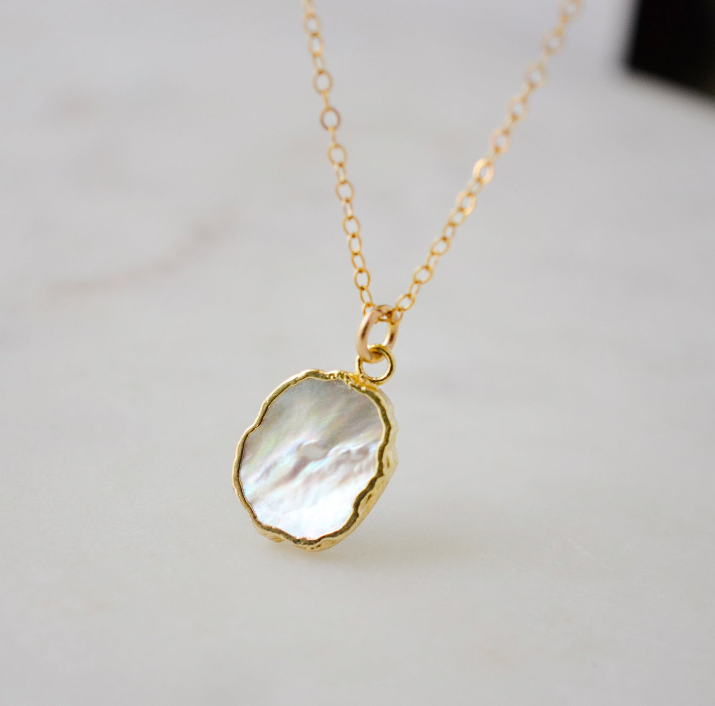 A smooth polished natural, white mother of pearl slice has been set in a 24k gold electroplated bezel and suspended from a 14k gold filled chain. The shell shimmers in shades of white, silver, and pink.
