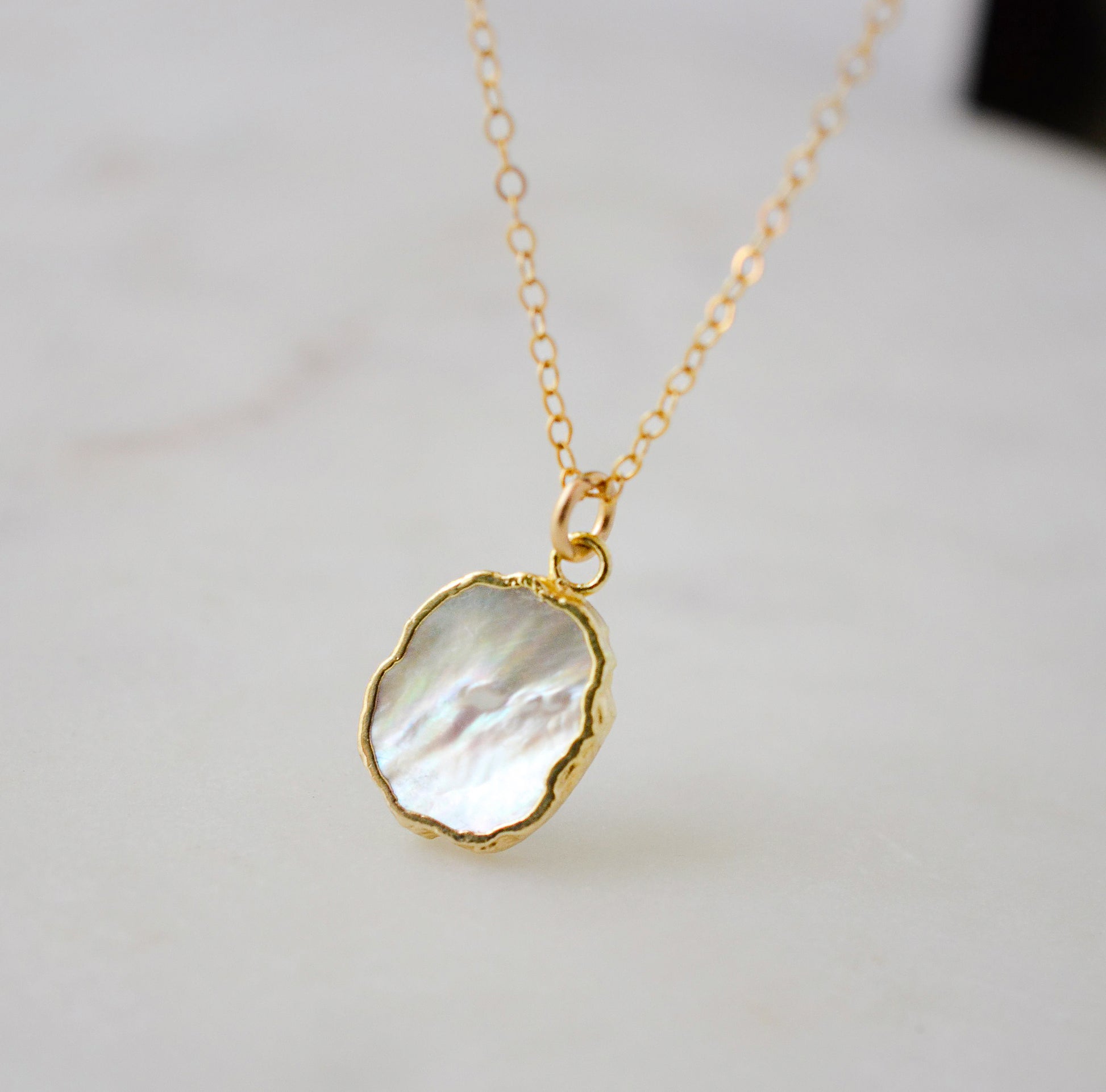 A smooth polished natural, white mother of pearl slice has been set in a 24k gold electroplated bezel and suspended from a 14k gold filled chain. The shell shimmers in shades of white, silver, and pink.