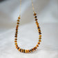 A close up image of genuine brown and gold tigereye gemstones set on a beaded necklace with a 14k gold filled chain. The stones are smooth polished semi-rondelle shape with tiny glass beads in between them. 