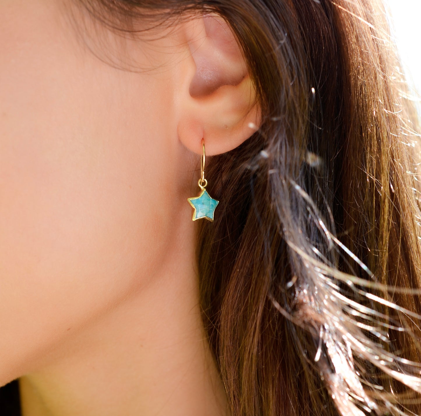 A woman wearing a dainty star earring handmade with blue turquoise and 14k gold filled. 