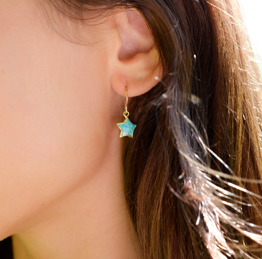 A woman wearing a dainty star earring handmade with blue turquoise and 14k gold filled. 