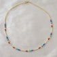 Tiny stones arranged in the order of the seven chakras or rainbow colors. Colors include: purple, blue, aqua, green, yellow, orange, and red. Close up of the gold style.