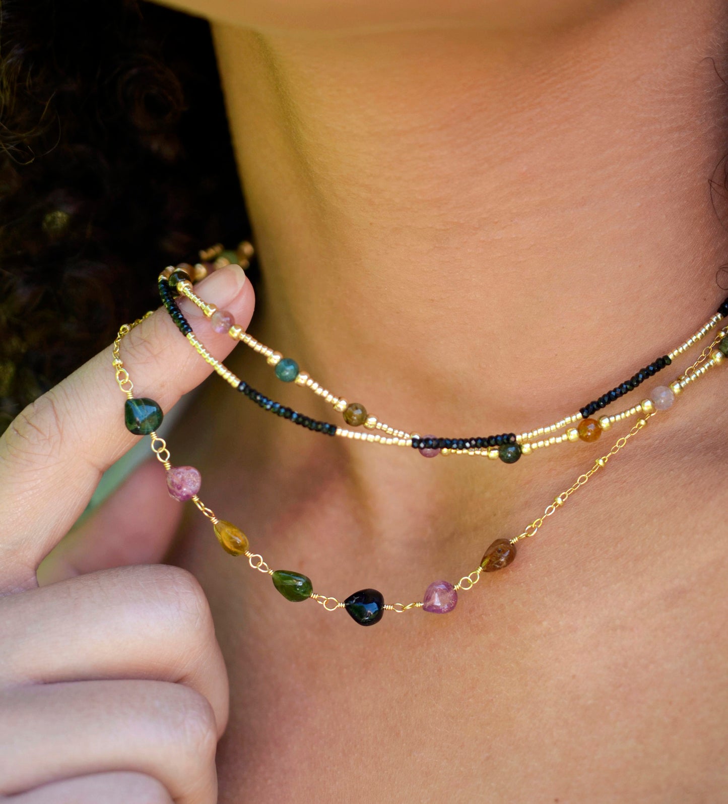Multi color Tourmaline drops chain necklace. Shown in gold. Stone colors include: pink, green, black, yellow, or brown. Close up modeled image. Shown with a beaded tourmaline and black onyx necklace.