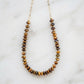 A beaded necklace made of polished tiger's eye beads on a delicate gold chain, displayed on a white marble surface. Handmade jewelry in USA by Gemnia.