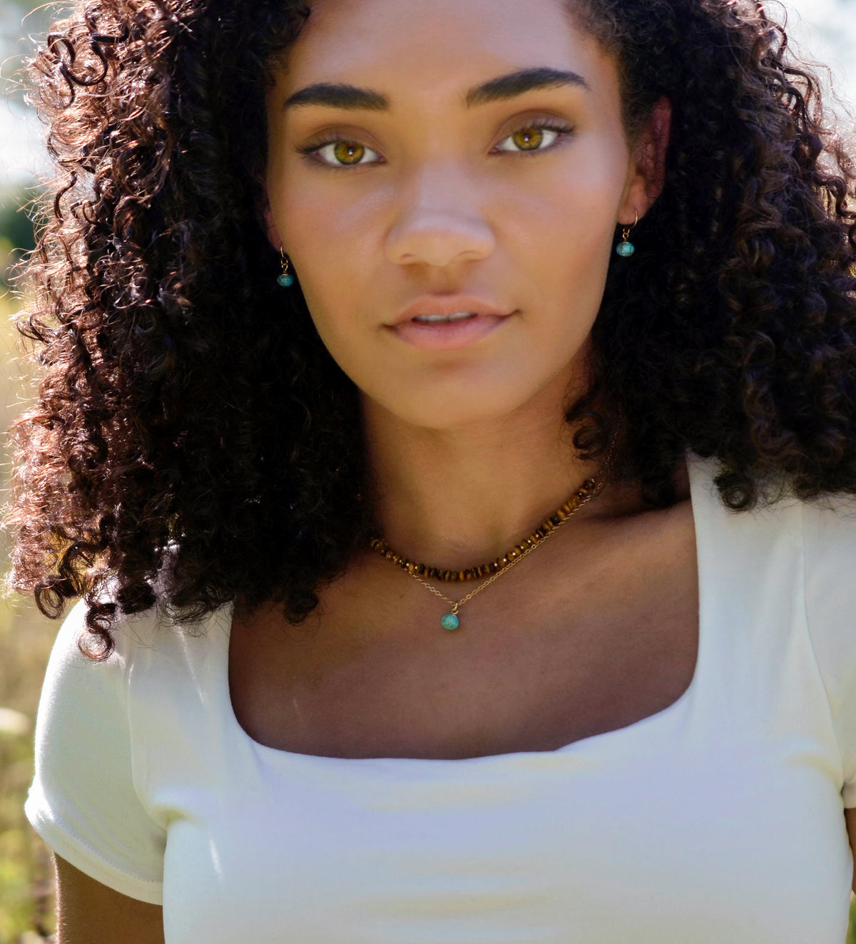 A woman wearing two layered necklaces of beaded tiger eye gemstones and natural blue turquoise drop pendant on 14k gold filled chain. Handmade in New England by Gemnia.