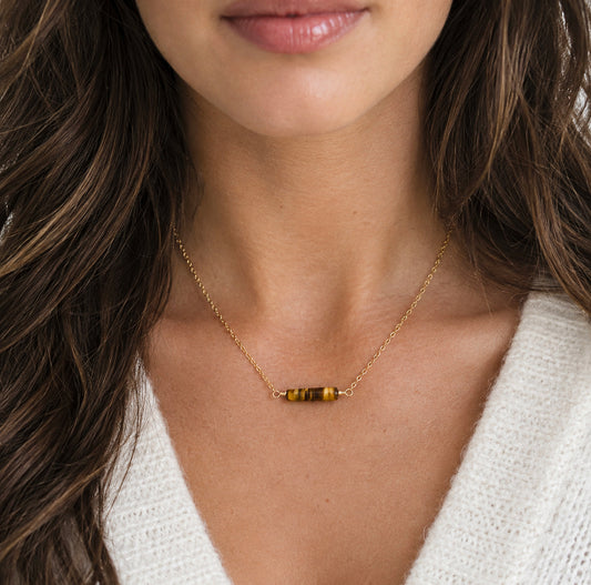 A close-up of a woman wearing a delicate gold chain necklace with a small horizontal bar of polished tiger's eye at the center. Handmade in Connecticut by Gemnia.