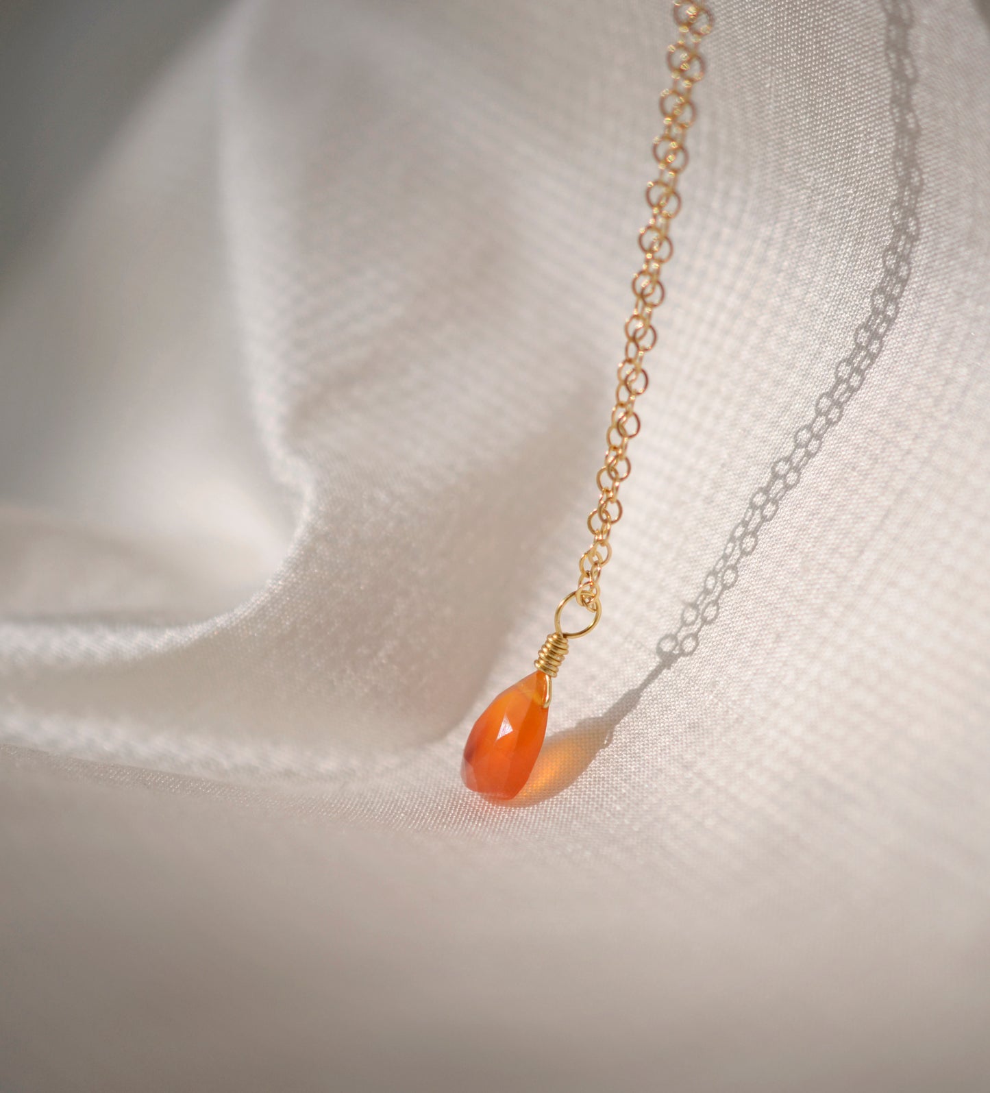 Natural orange triangular shaped Carnelian gemstone set onto a gold chain. Side view.