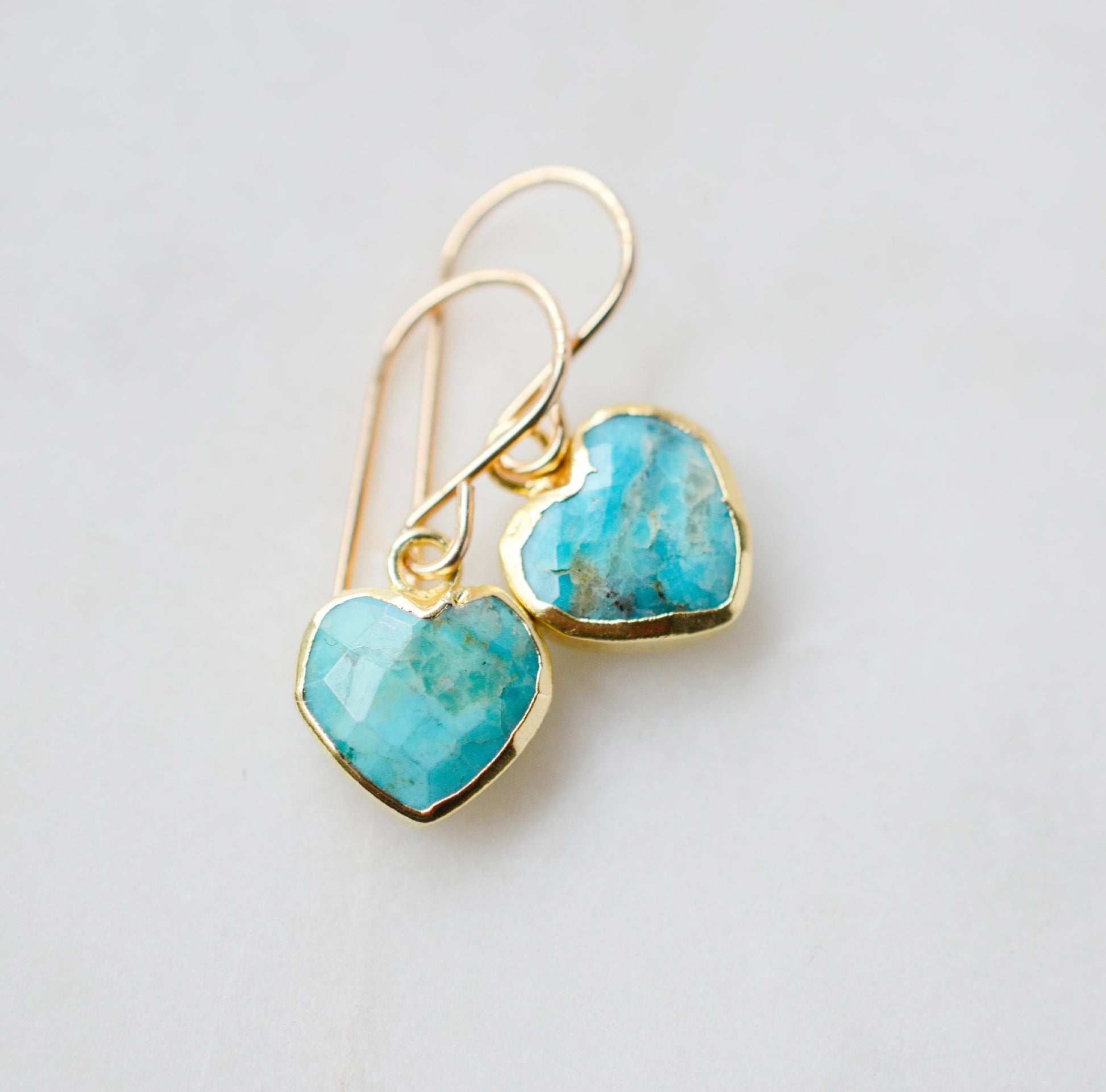 Genuine, natural blue turquoise faceted hearts set on 14k gold filled earring hooks. The stones range in blue and green, with some containing white or brown.