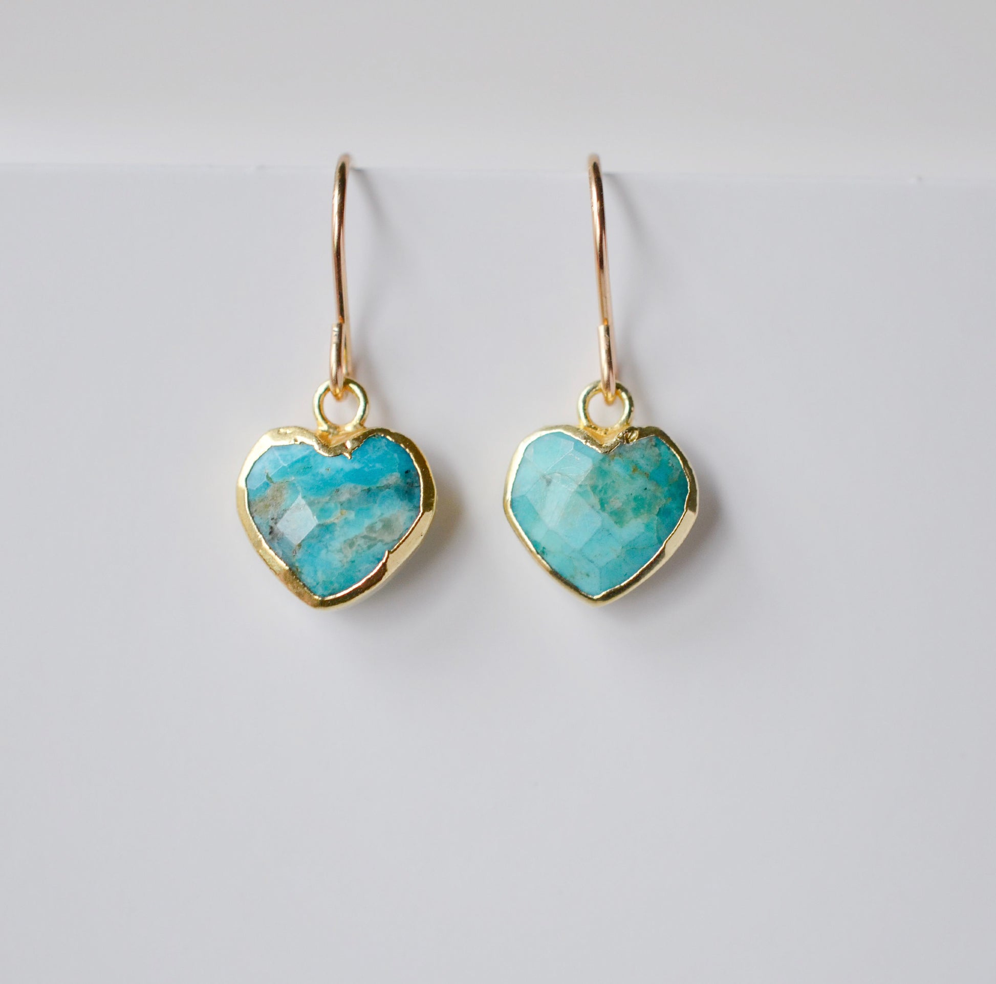 Genuine, natural blue turquoise faceted hearts set on 14k gold filled earring hooks. The stones range in blue and green, with some containing white or brown.