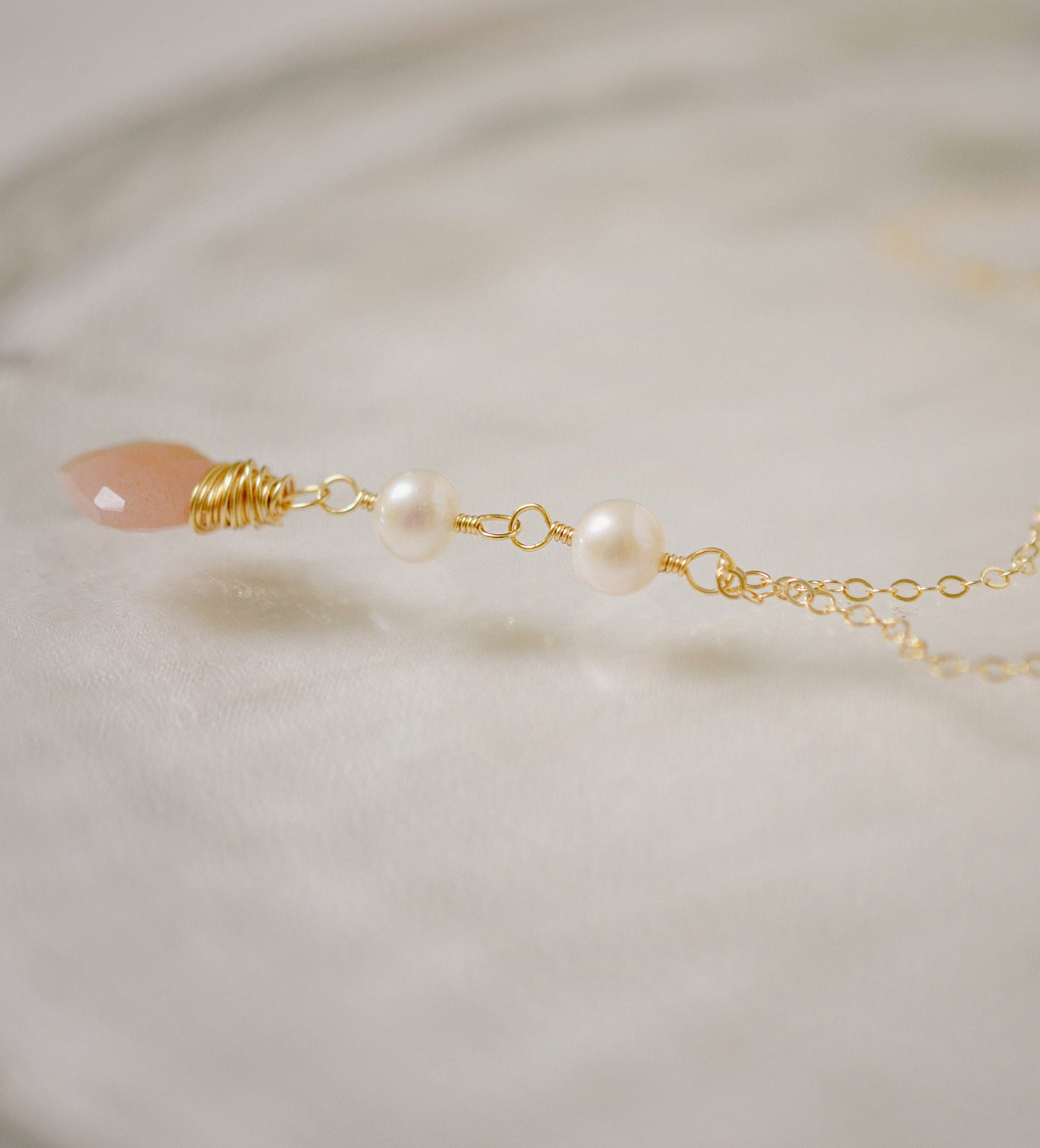 Side View. Two white semi-round pearls hang over a natural peach Moonstone faceted drop. The gold style pendant is shown.