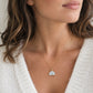 A close-up of a woman wearing a delicate gold chain necklace with a small, semi-circular white pendant featuring a natural sparkling white quartz druzy. Handmade in Connecticut by Gemnia.