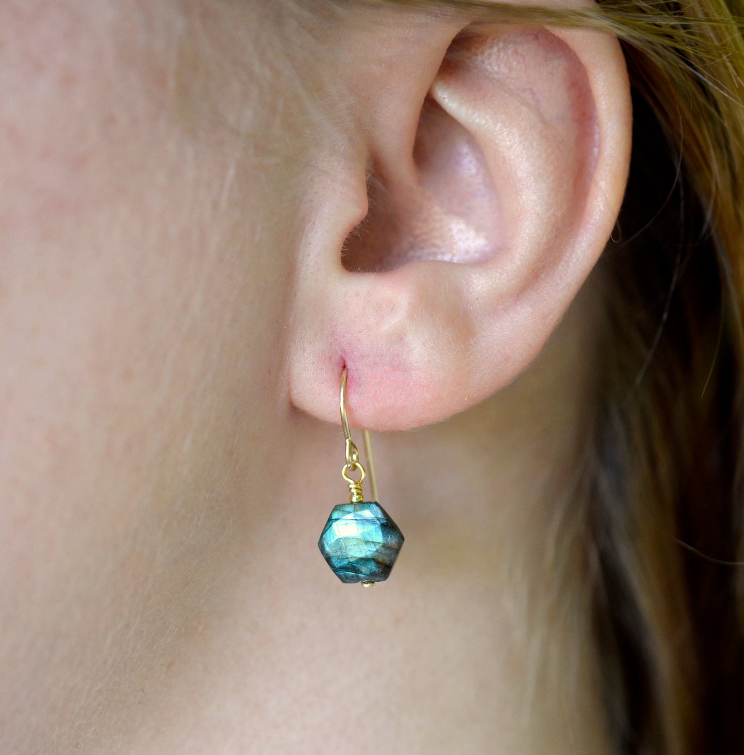 Blue flashing Labradorite gemstones in a faceted hexagonal shape dangle from 14k gold filled earring hooks. Small gold beads accent below the stone. Also available in sterling silver. Modeled image.