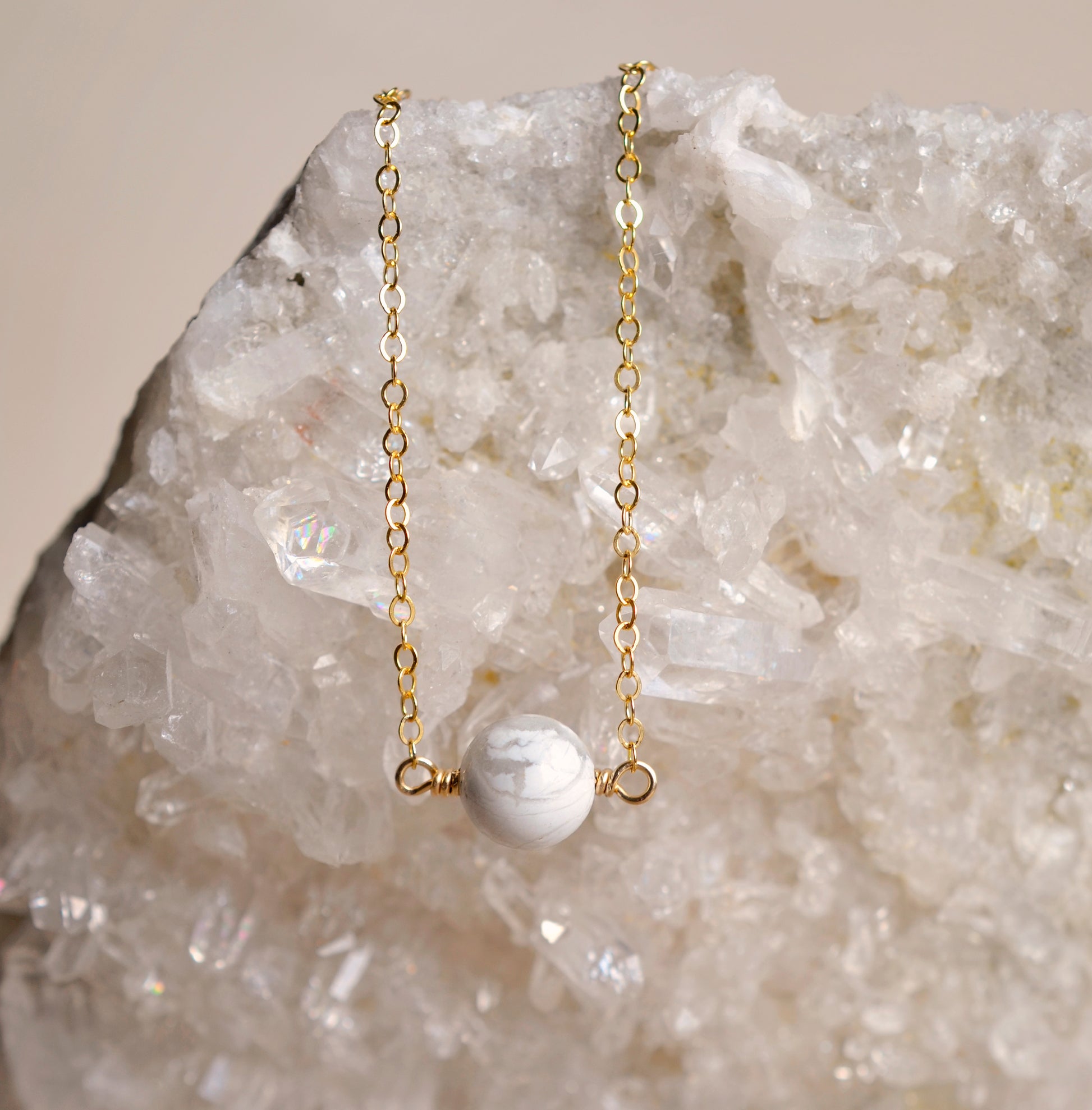 A natural white howlite necklace on a crystal quartz background. The stone is round with natural gray marbling and set on a 14k gold filled chain. Also available in sterling silver. 