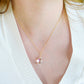 A woman wearing a clear, faceted mystic topaz teardrop pendant with shimmering rainbow colors within the gemstone. This dainty necklace is set on a simple 14k gold filled chain. Handmade jewelry in Connecticut by Gemnia.