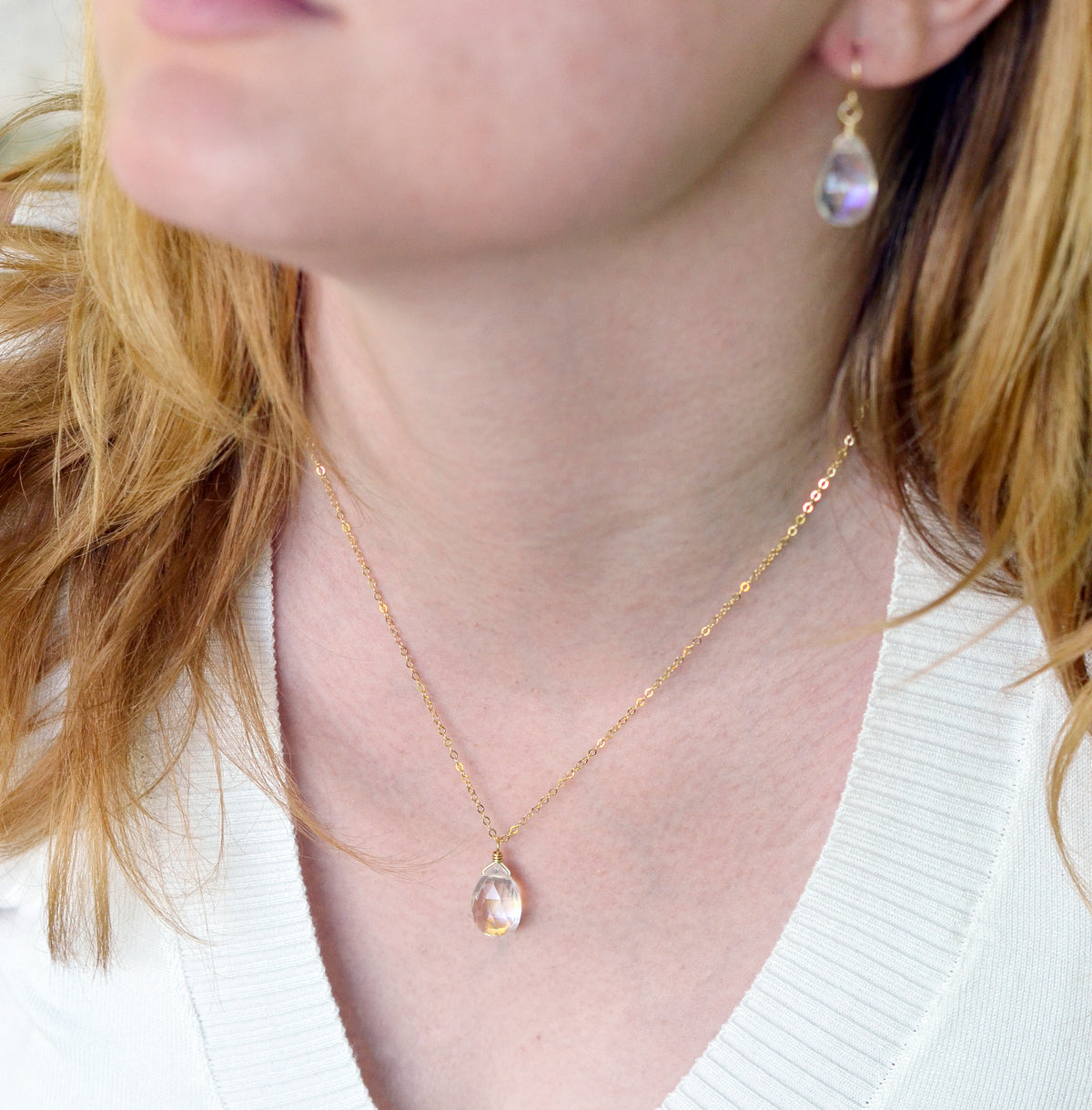 A woman wearing a dainty, but very sparkly rainbow mystic topaz faceted teardrop pendant suspended from a 14k gold filled cable chain. She is also wearing matching earrings. This piece is available in sterling silver, as well.