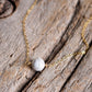 A white howlite necklace on a wood background. The stone is round with natural gray marbling and set on a 14k gold filled chain. Also available in sterling silver. 
